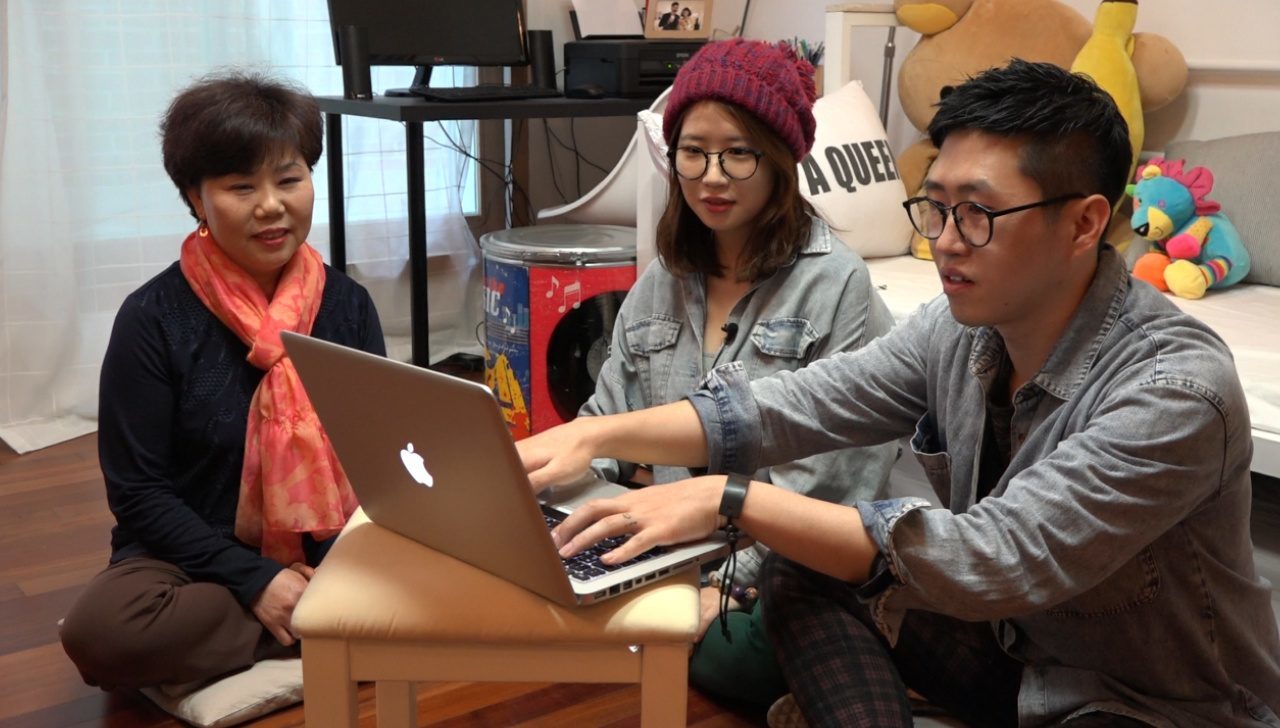 Jeon Je-woo (right) shows his mom (left) a Prezi in *One Way Ticket*.